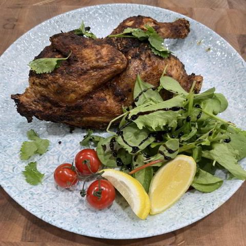 A beautifully grilled chicken with some greens and vine tomatoes.